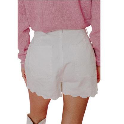 White shorts with scalloped hem worn by a person in a pink sweater on a white background