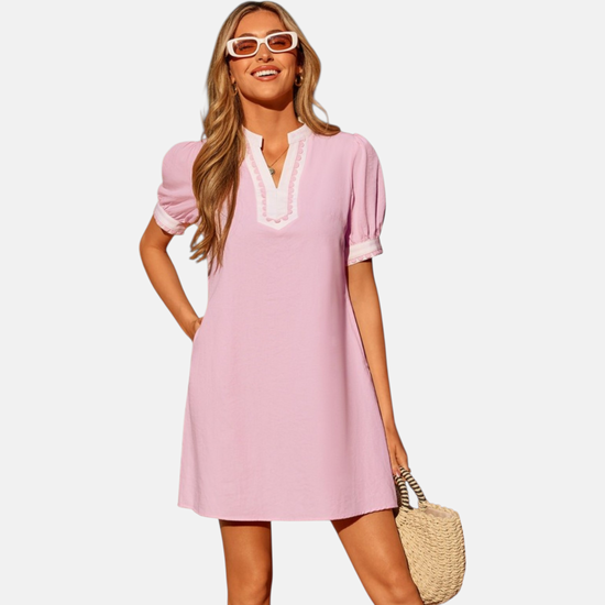 Woman wearing a pink dress with white trim on a plain background