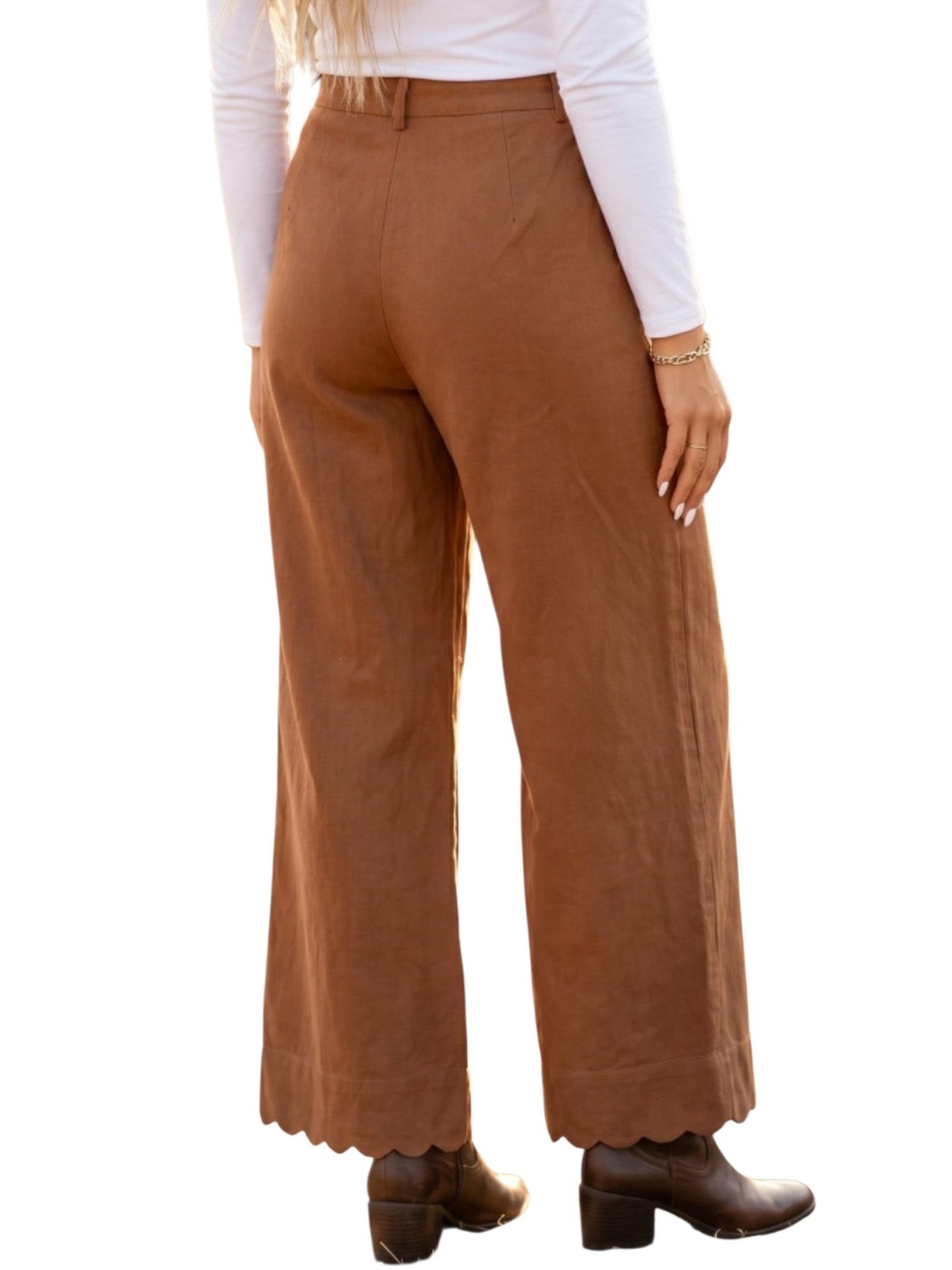 A person shown from the back wearing high-waisted, wide-leg brown pants with a scalloped hem, paired with a white long-sleeve top and dark brown ankle boots, against a plain white background.