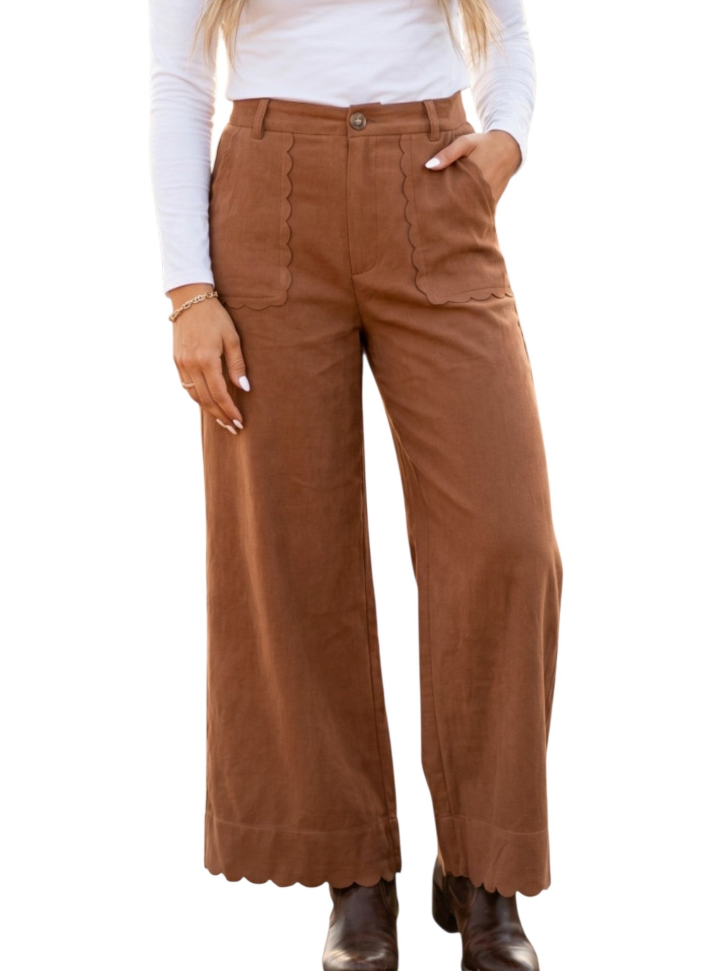 A person wearing high-waisted brown wide-leg pants with scalloped hems and front patch pockets, styled with a white long-sleeve top and dark brown ankle boots against a plain white background.