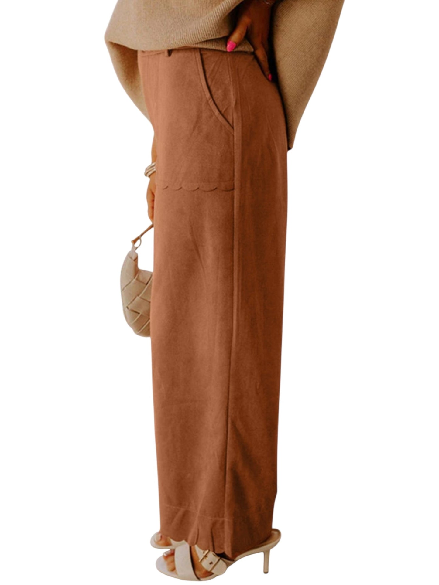 A person wearing a pair of wide-leg brown pants with a textured fabric finish, styled with a beige top, beige sandals, and a small woven handbag against a plain white background.