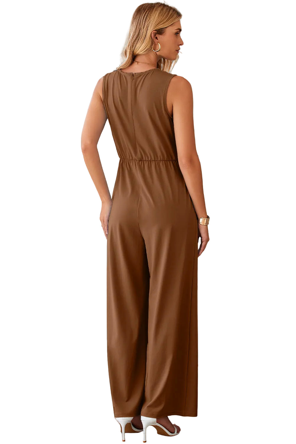Woman wearing a brown jumpsuit standing in a modern indoor setting against a white background