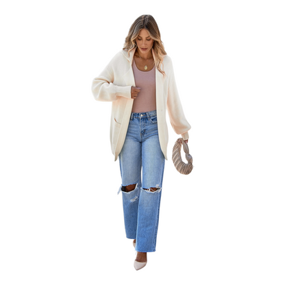 Woman wearing a cream cardigan, pink top, and blue jeans on a white background