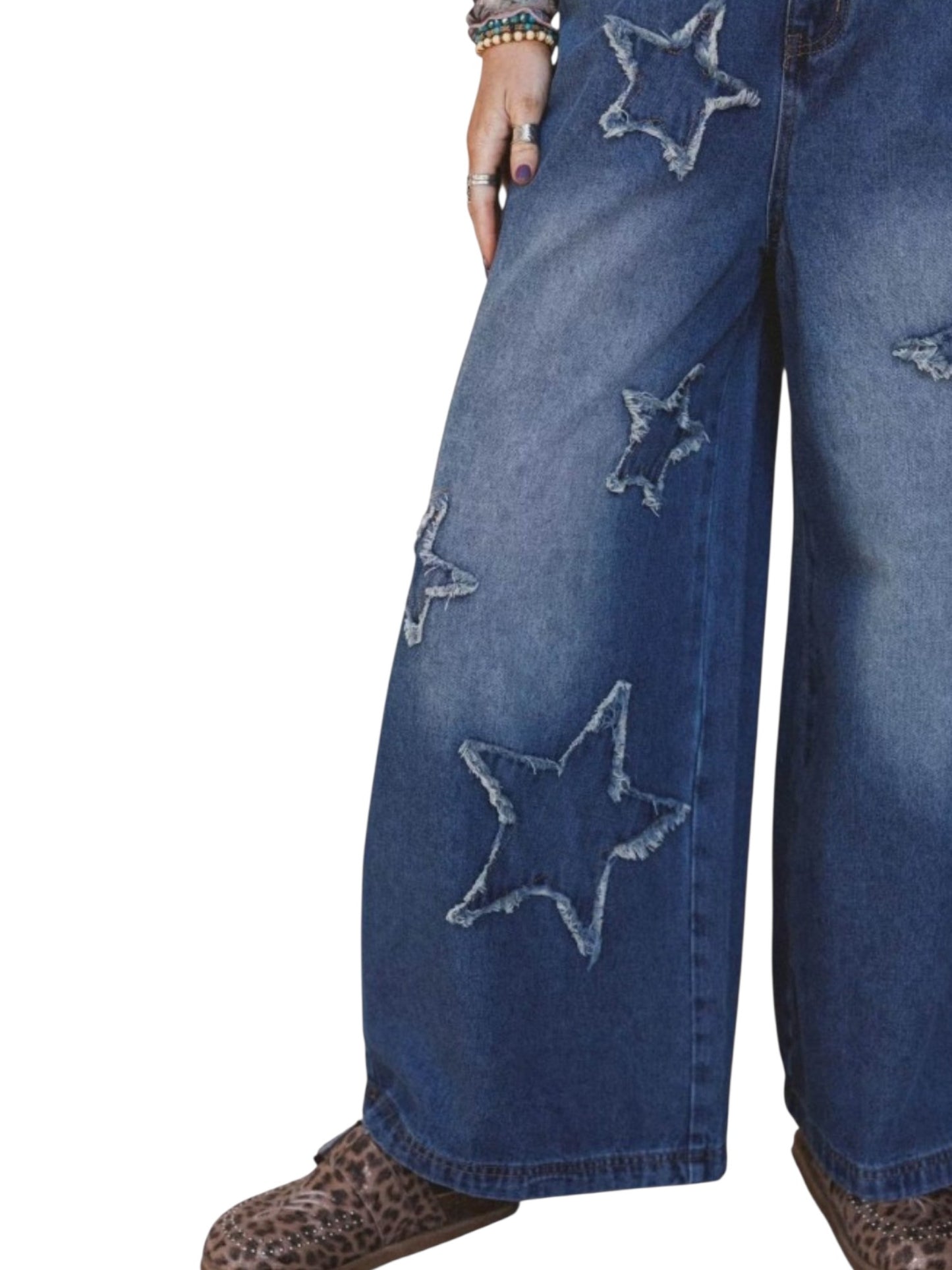 Close-up of a person wearing wide-leg blue denim jeans with large embroidered star patches on the legs, paired with leopard-print shoes against a white background.