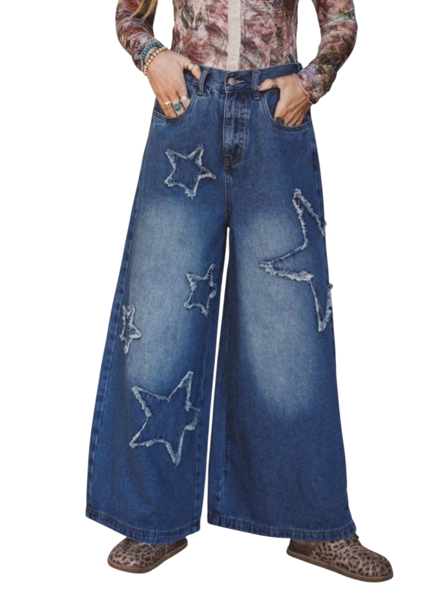 A person wearing wide-leg blue denim jeans with large embroidered star patches on the front, paired with a patterned long-sleeve top and leopard-print shoes, shown against a plain white background.