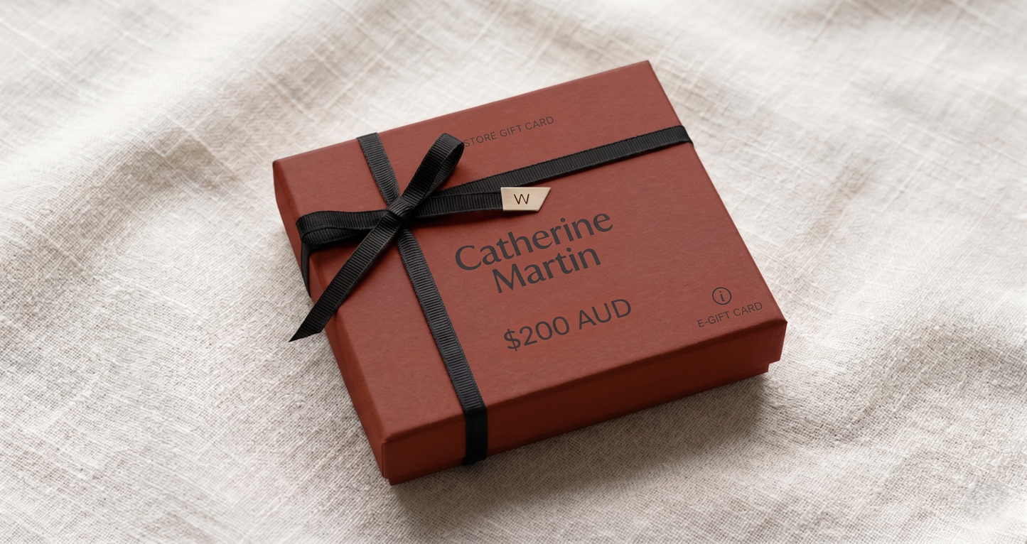 Red gift box with black ribbon and 'Catherine Martin' branding on a textured surface