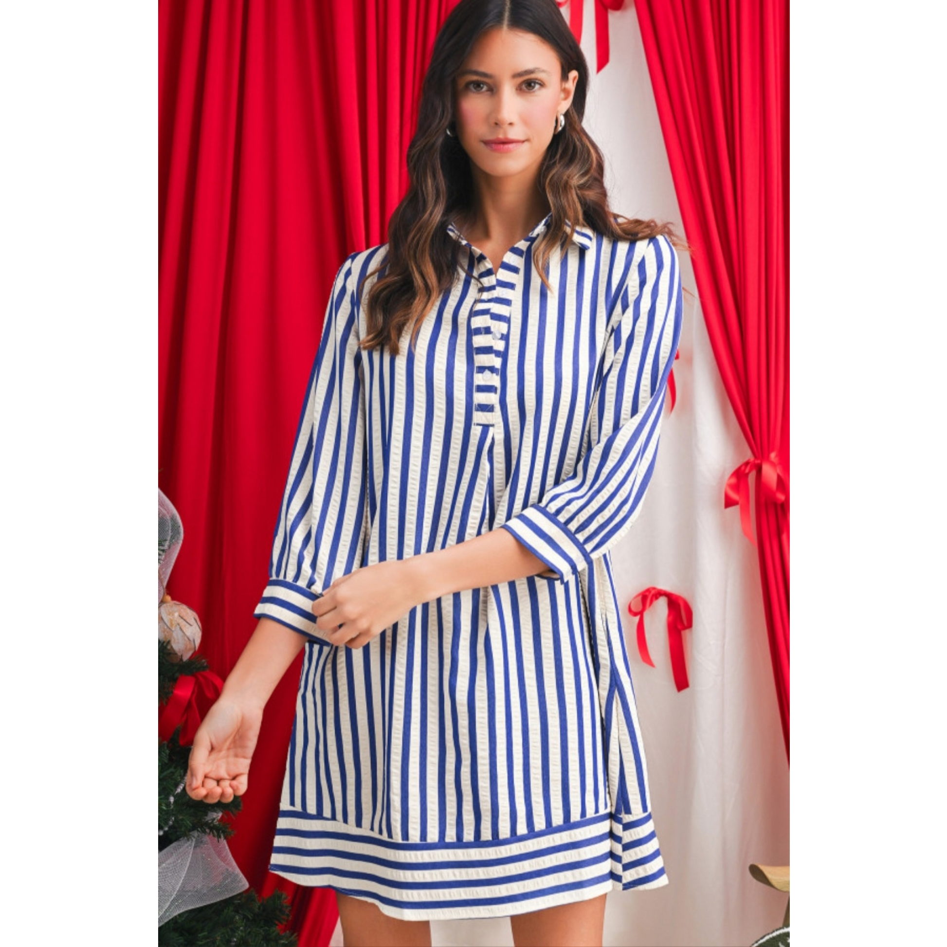 Woman wearing a blue and white striped dress in front of red curtains.