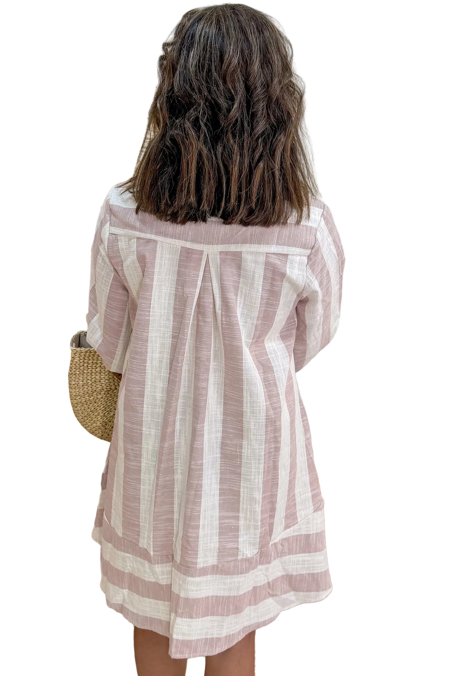 A child viewed from behind wearing a loose, short-sleeve striped tunic or dress in dusty pink and off-white, standing against a white background
