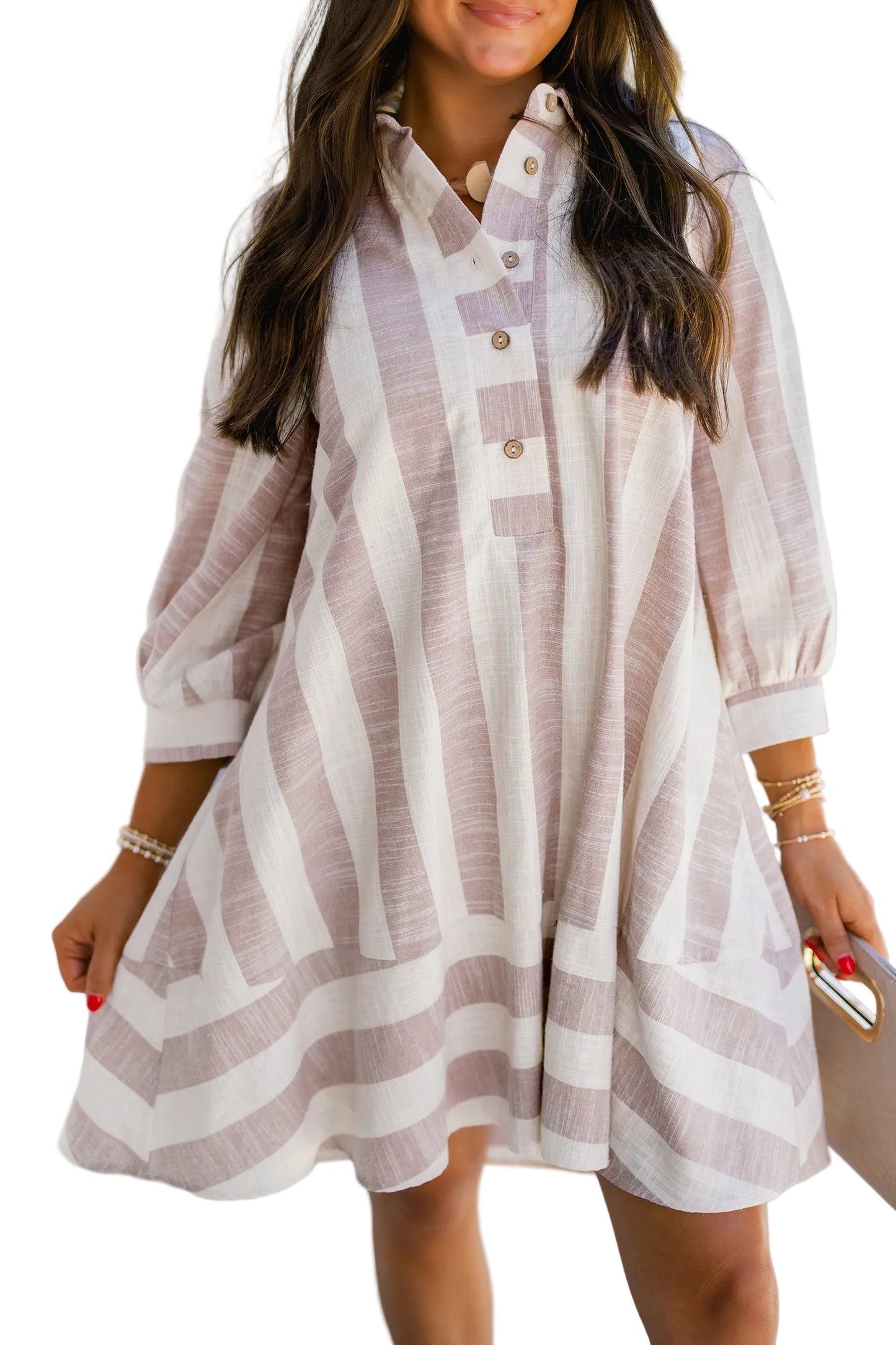 A woman wearing a loose, long-sleeve button-front dress with vertical blush pink and off-white stripes, photographed in against a white background