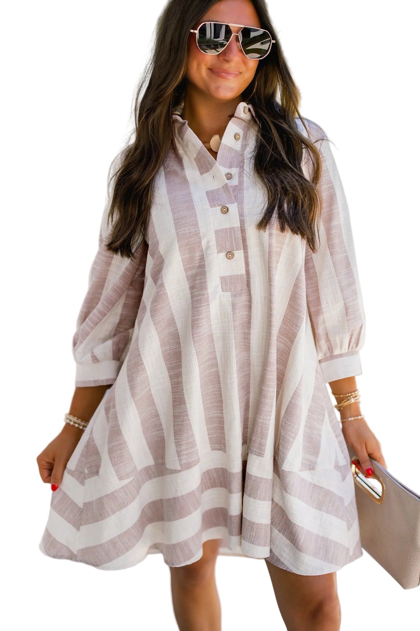 Woman wearing a striped dress with sunglasses and holding a clutch against a white background.