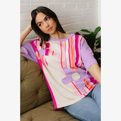 Woman wearing a colorful striped shirt with a flower design, sitting on a couch.