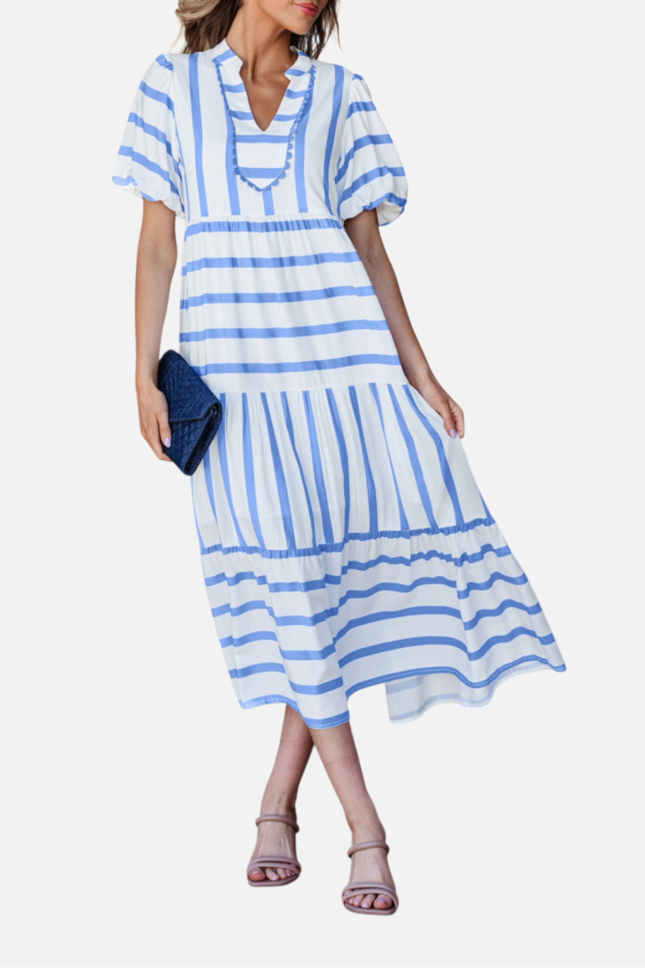 A model showcasing the sky blue striped midi dress, featuring a notched V-neckline with blue ricrac trim, puff sleeves, and a tiered skirt in a vacation-ready 100% viscose fabric.