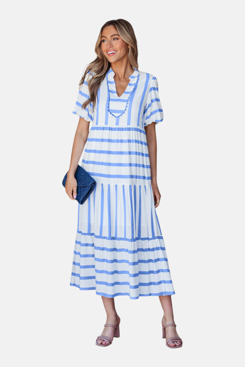 A model showcasing the sky blue striped midi dress, featuring a notched V-neckline with blue ricrac trim, puff sleeves, and a tiered skirt in a vacation-ready 100% viscose fabric.