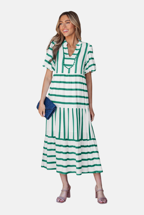 A model showcasing the green striped midi dress, featuring a notched V-neckline with blue ricrac trim, puff sleeves, and a tiered skirt in a vacation-ready 100% viscose fabric.