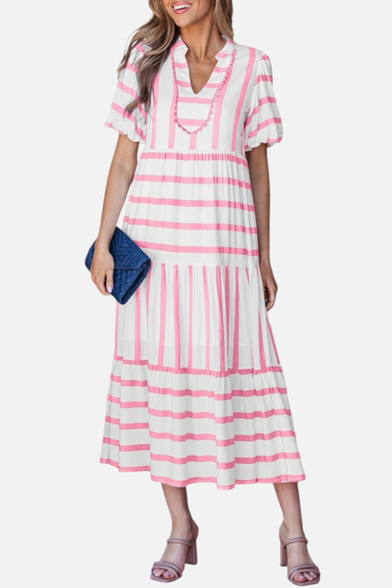 A model showcasing the pink striped midi dress, featuring a notched V-neckline with pink ricrac trim, puff sleeves, and a tiered skirt in a vacation-ready 100% viscose fabric.