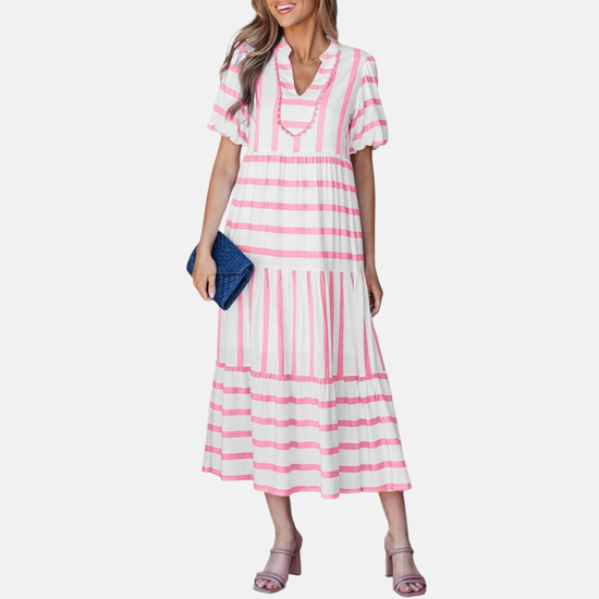 A model showcasing the pink striped midi dress, featuring a notched V-neckline with pink ricrac trim, puff sleeves, and a tiered skirt in a vacation-ready 100% viscose fabric.