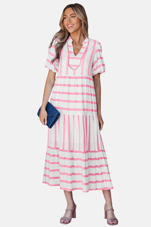 A model showcasing the pink striped midi dress, featuring a notched V-neckline with pink ricrac trim, puff sleeves, and a tiered skirt in a vacation-ready 100% viscose fabric.