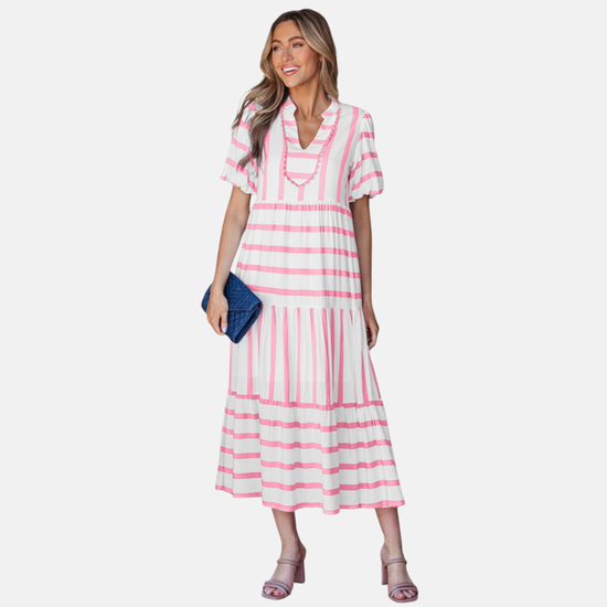 A model showcasing the pink striped midi dress, featuring a notched V-neckline with pink ricrac trim, puff sleeves, and a tiered skirt in a vacation-ready 100% viscose fabric.
