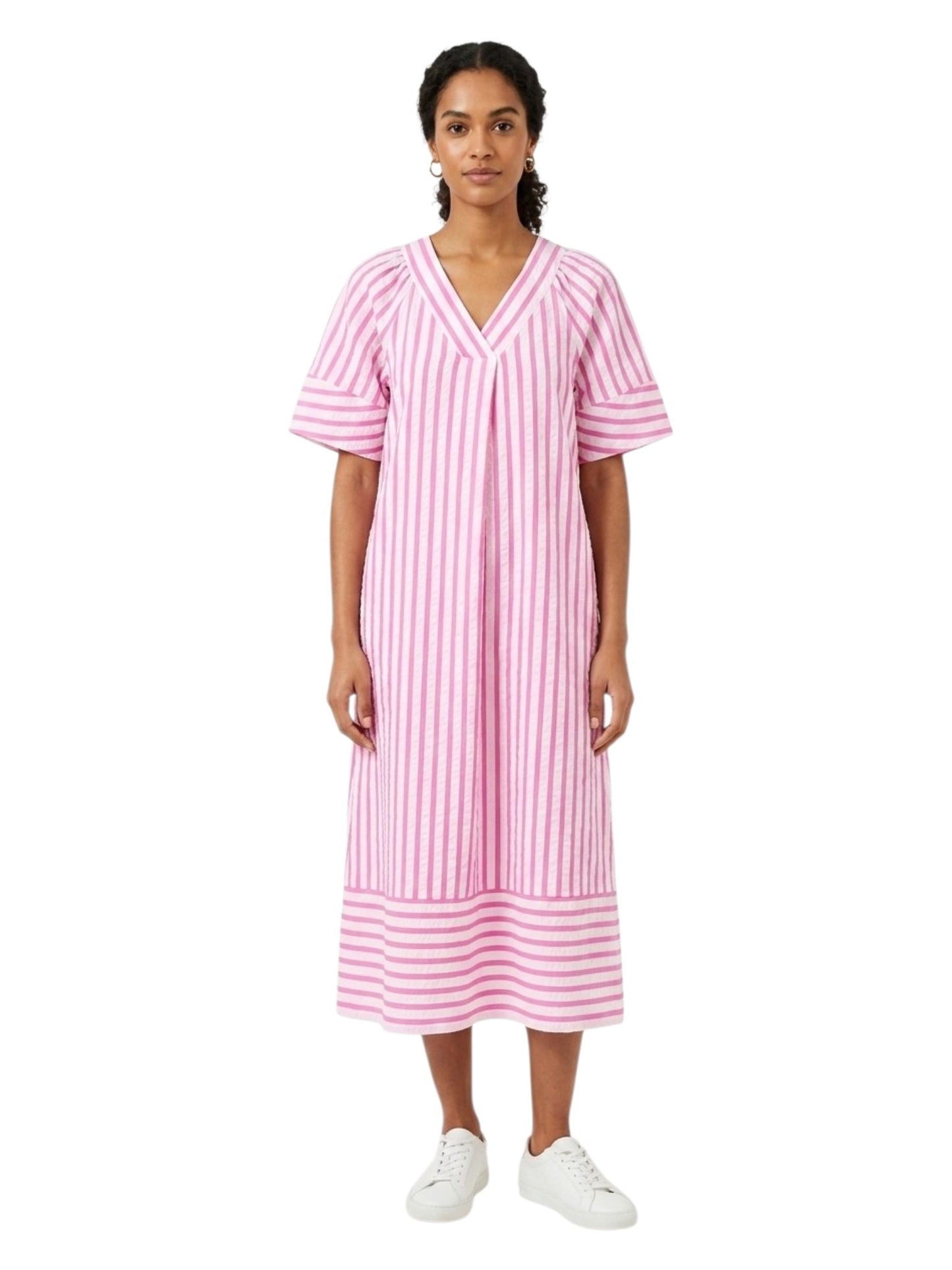 A woman modeling a pink and white vertically striped short-sleeve midi dress with a V-neckline, paired with white sneakers, against a plain white background.