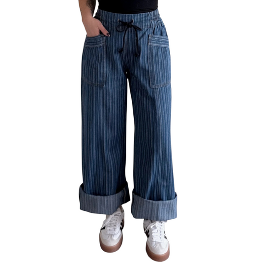 Person wearing wide-leg, blue pinstriped drawstring pants with cuffed hems, paired with white sneakers.