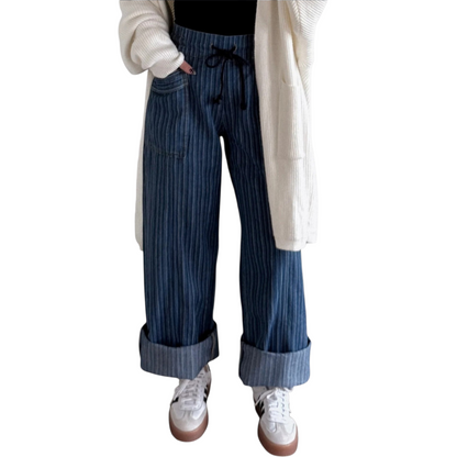 Person wearing wide-leg, blue pinstriped drawstring pants with cuffed hems, paired with white sneakers and white cardigan.