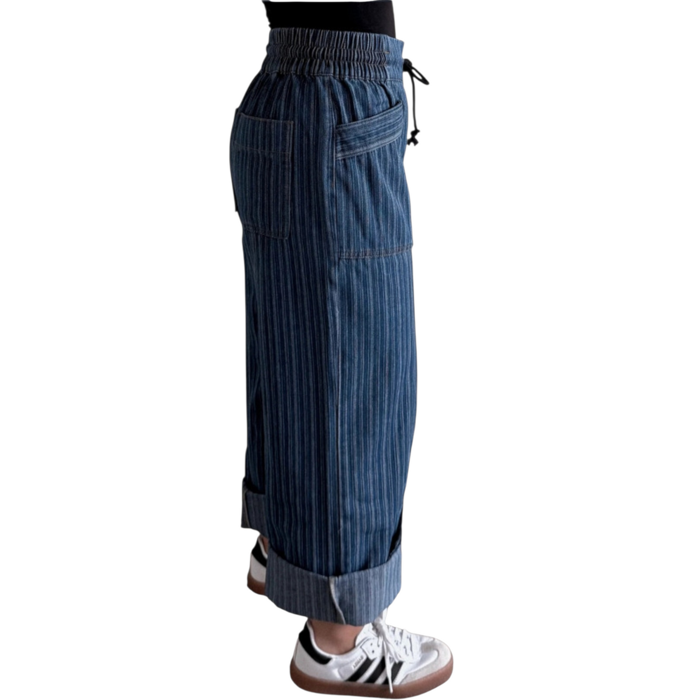 Person wearing wide-leg, blue pinstriped drawstring pants with cuffed hems, paired with white sneakers. Viewing from the right side.