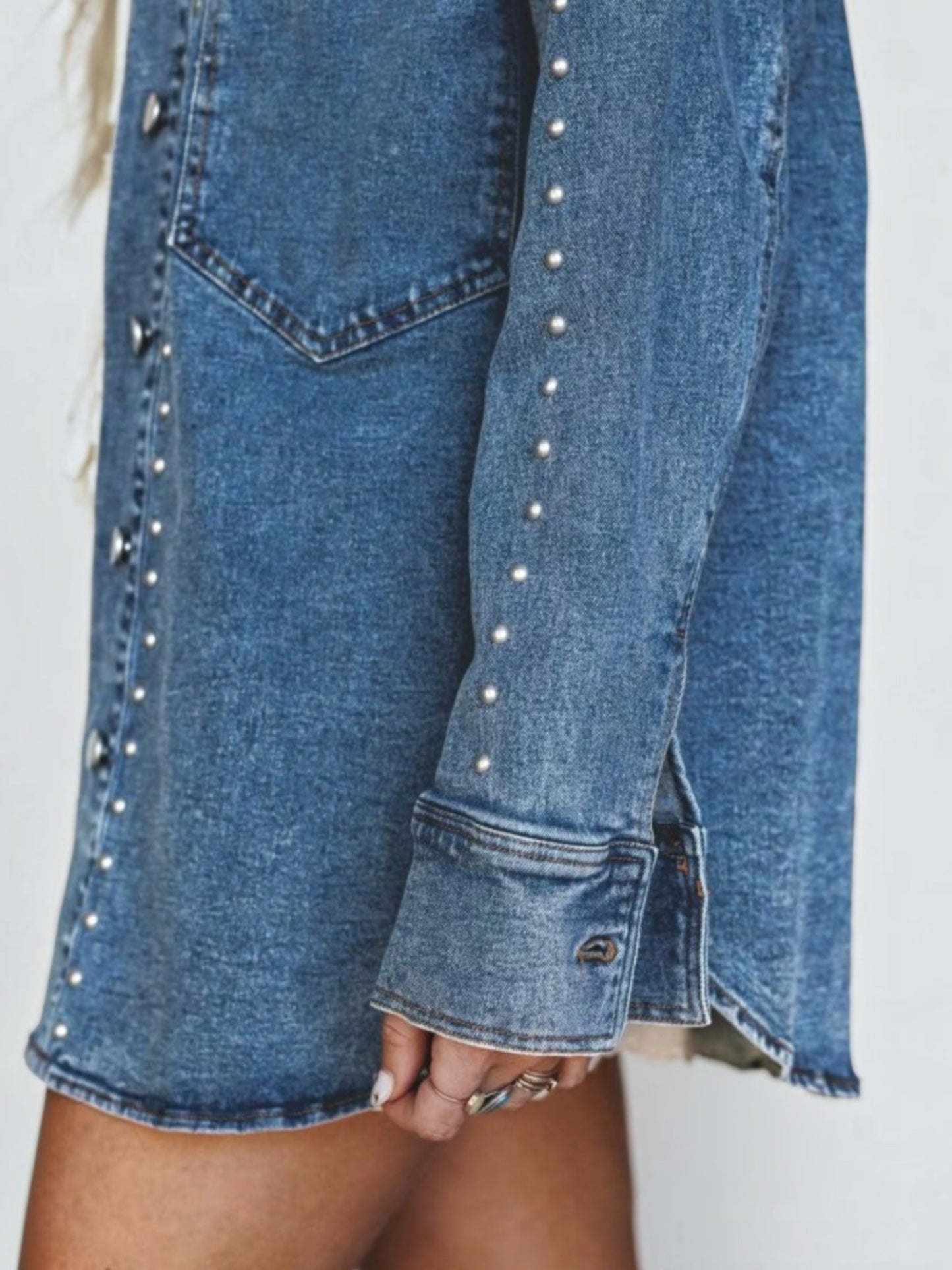 Close-up of a blue denim shirt dress with silver stud embellishments along the front and cuffs, worn by a model.