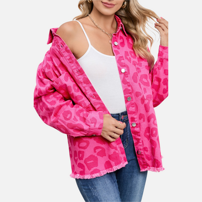 A 3/4 front view of a woman wearing the unbuttoned pink leopard print denim jacket over blue jeans, demonstrating the product’s vibrant color and relaxed, contemporary fit.