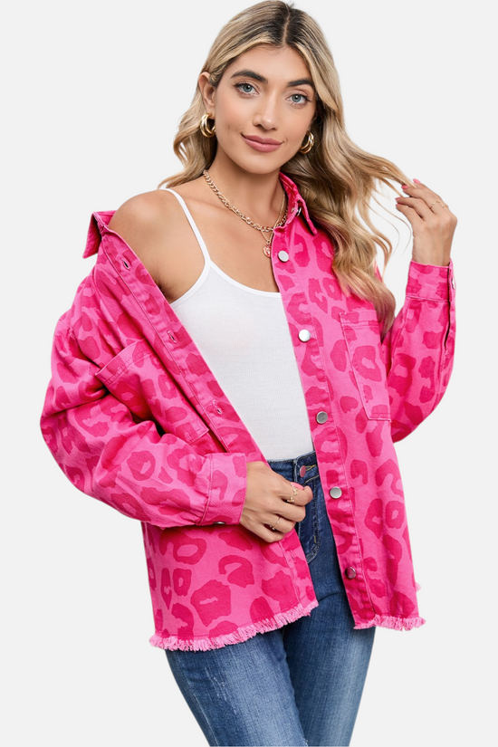 A model confidently poses in the unbuttoned pink leopard print denim jacket, revealing a white camisole and blue jeans, perfect for showing versatile layering and casual style.