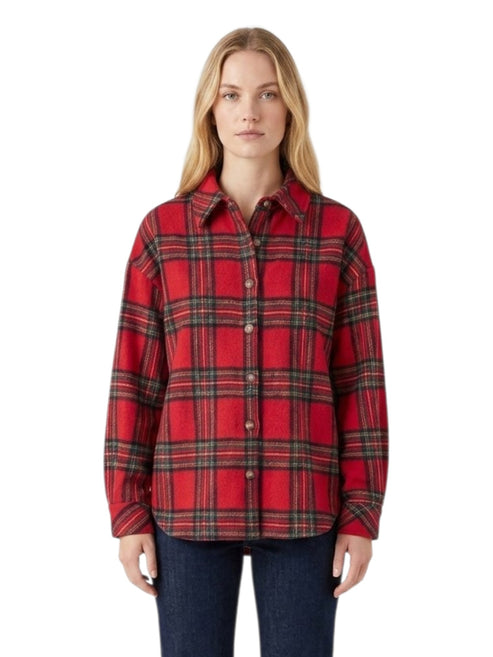 A woman modeling a red long-sleeve plaid button-up shirt with dark green and black stripes, paired with dark blue jeans, against a plain white background.