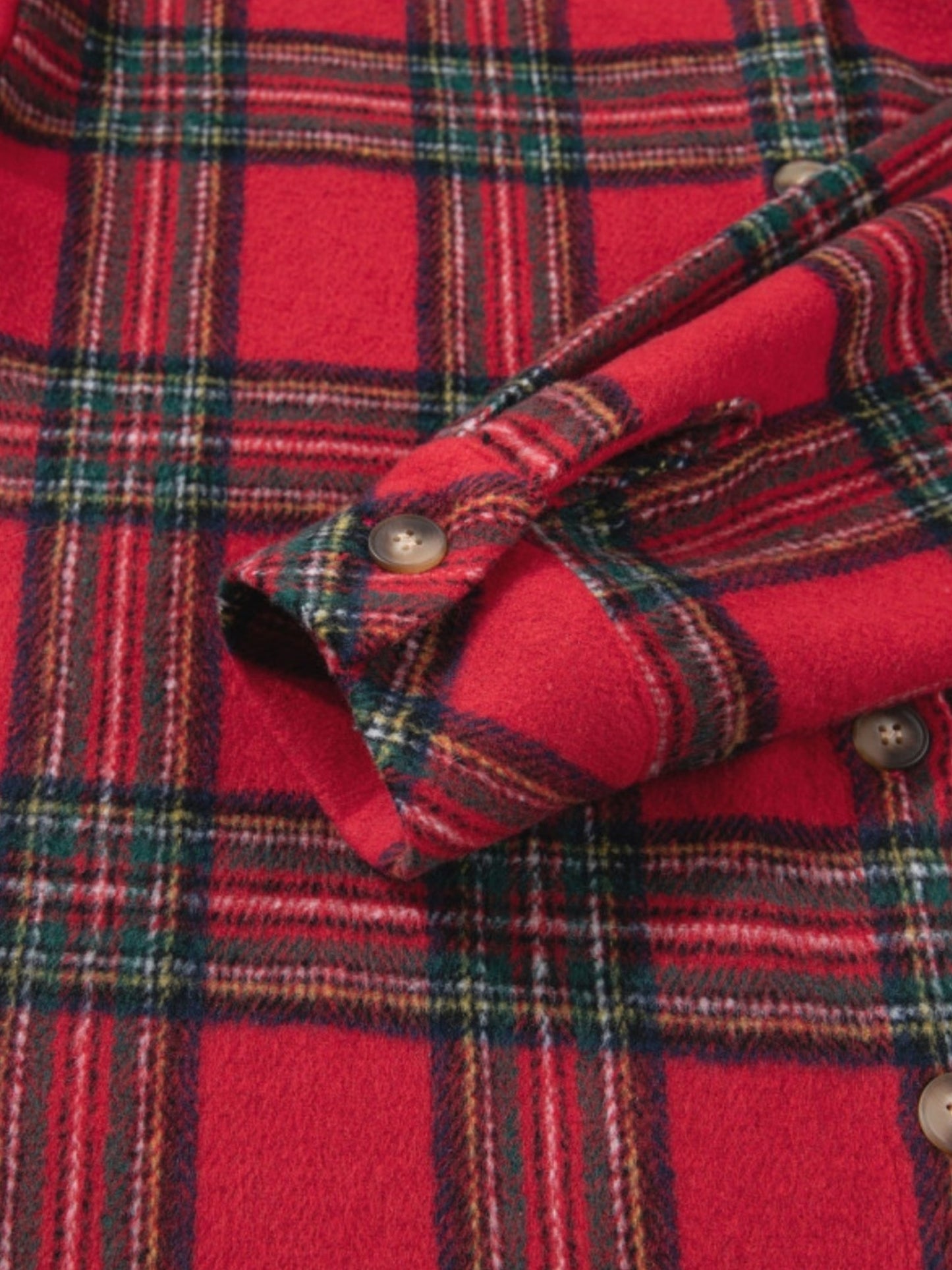 Close-up of a red plaid flannel shirt with green, yellow, and white stripes, showing the buttoned cuff and fabric texture.