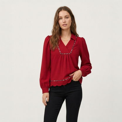 Close-up studio shot of a model wearing a red textured collared blouse, highlighting the leopard print trim on the V-neckline.