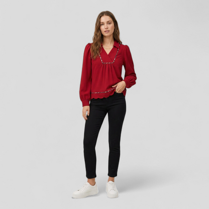 A model standing in a red long-sleeved textured blouse with leopard print trim, styled with black skinny jeans and white sneakers.