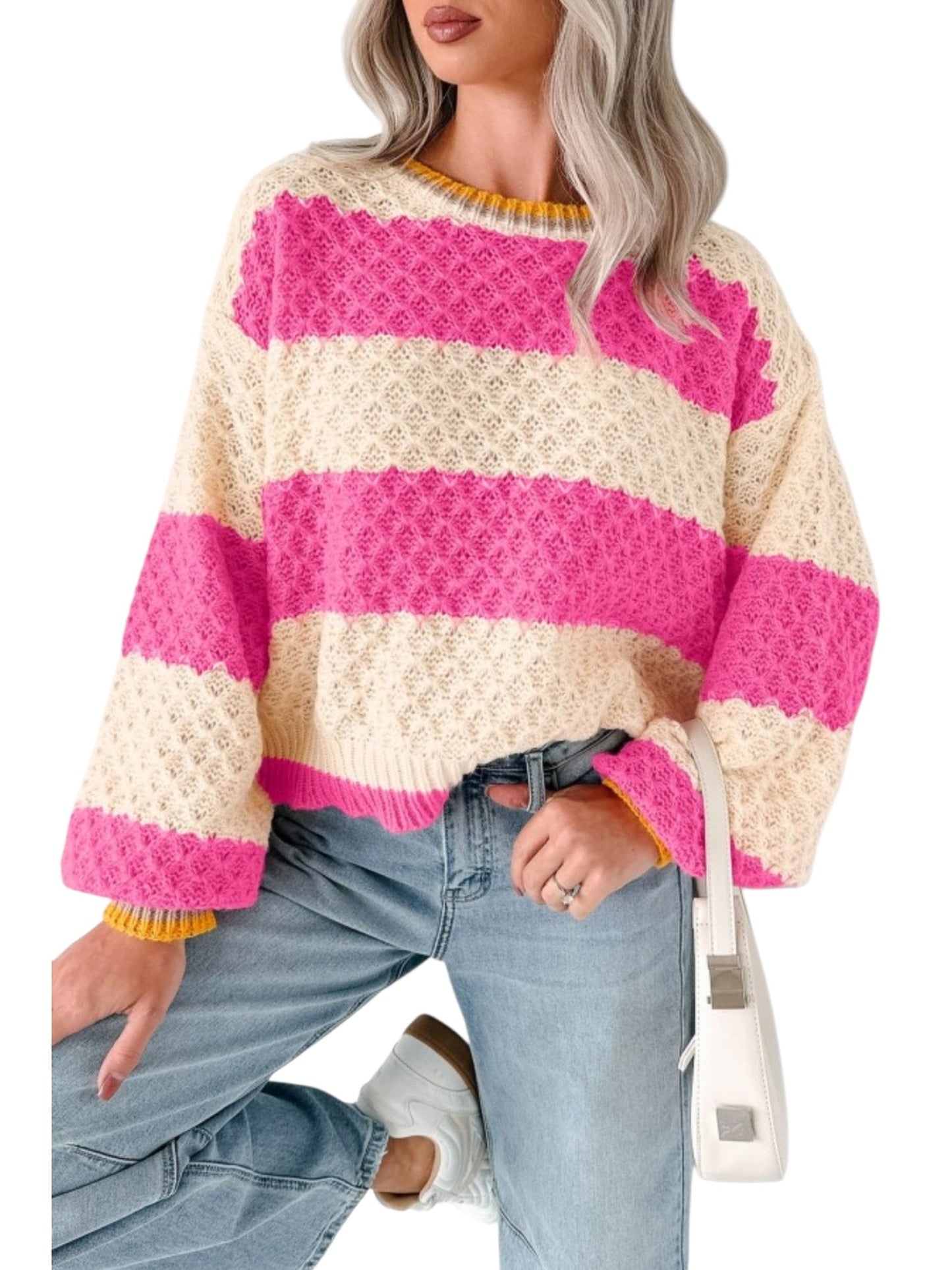 A woman wearing a chunky knit sweater with bold horizontal stripes in cream and bright pink, paired with light blue jeans and a white shoulder bag.