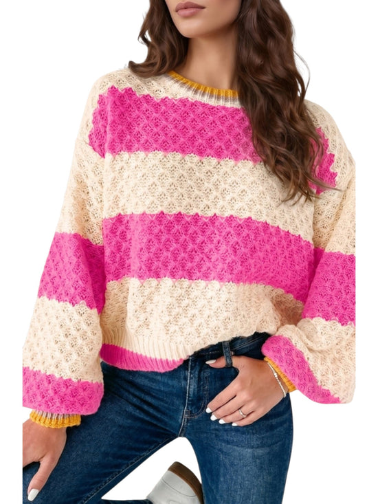 A woman wearing a cream and bright pink striped knit sweater with textured knit patterns and yellow ribbed trim at the collar and cuffs, paired with blue jeans.