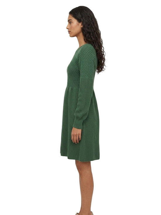 A woman shown in side profile wearing a green ribbed knit long-sleeve dress against a plain white background.