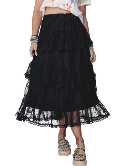 A black tiered tulle maxi skirt with a ruffled hem, shown on a model wearing a white floral crop top and woven sandals against a white background.