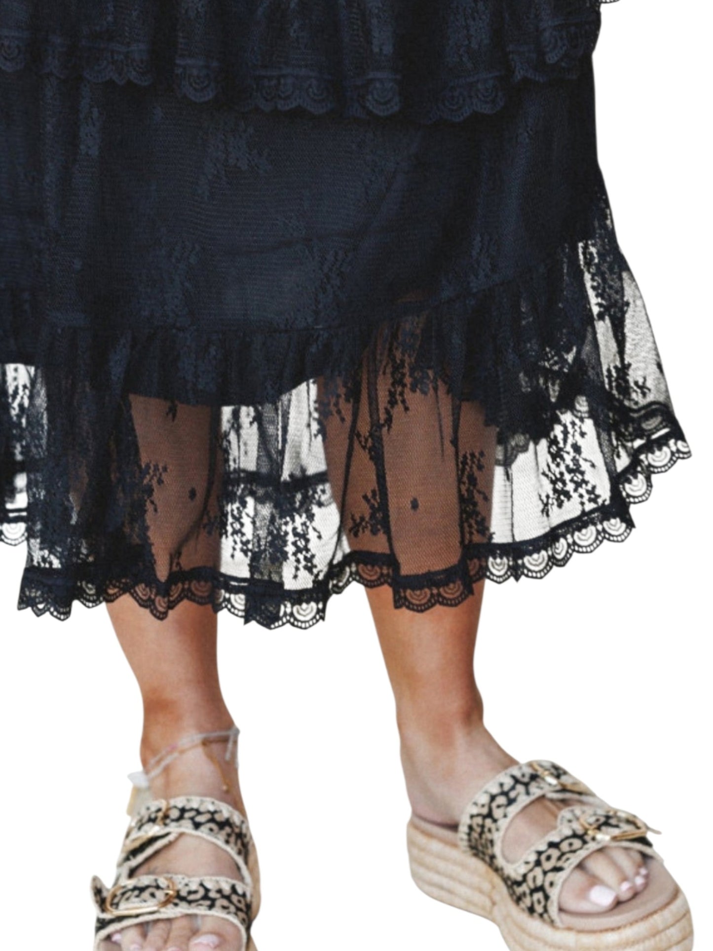 A close-up of a person wearing a black lace tiered skirt with sheer mesh and patterned black-and-beige platform sandals against a plain white background.