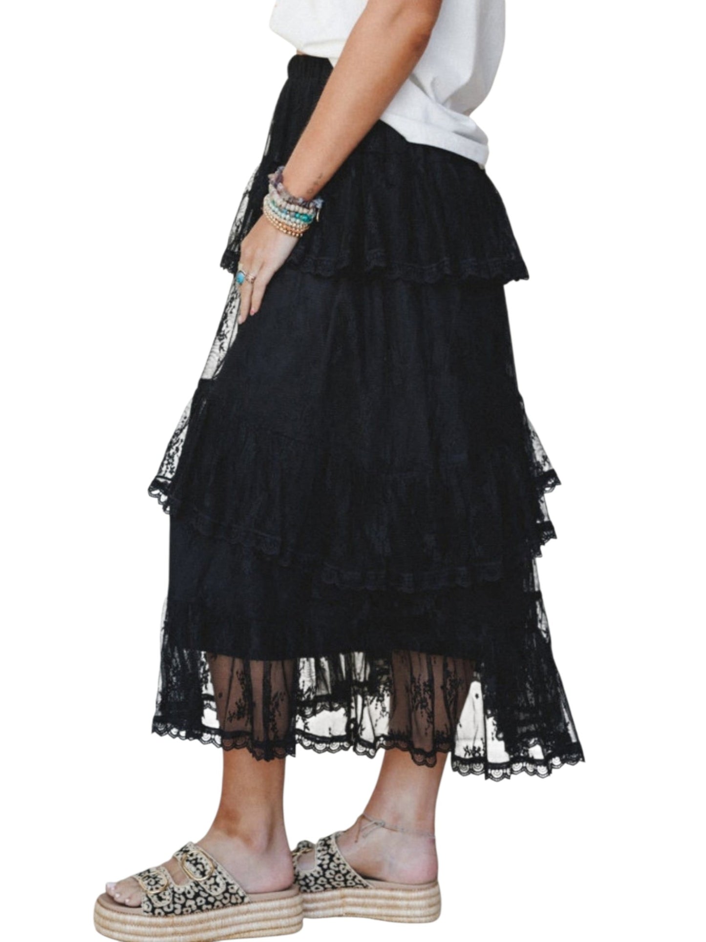 A black tiered ruffle midi skirt with sheer lace trim, shown on a model wearing a white top and espadrille-style slide sandals against a plain white background.