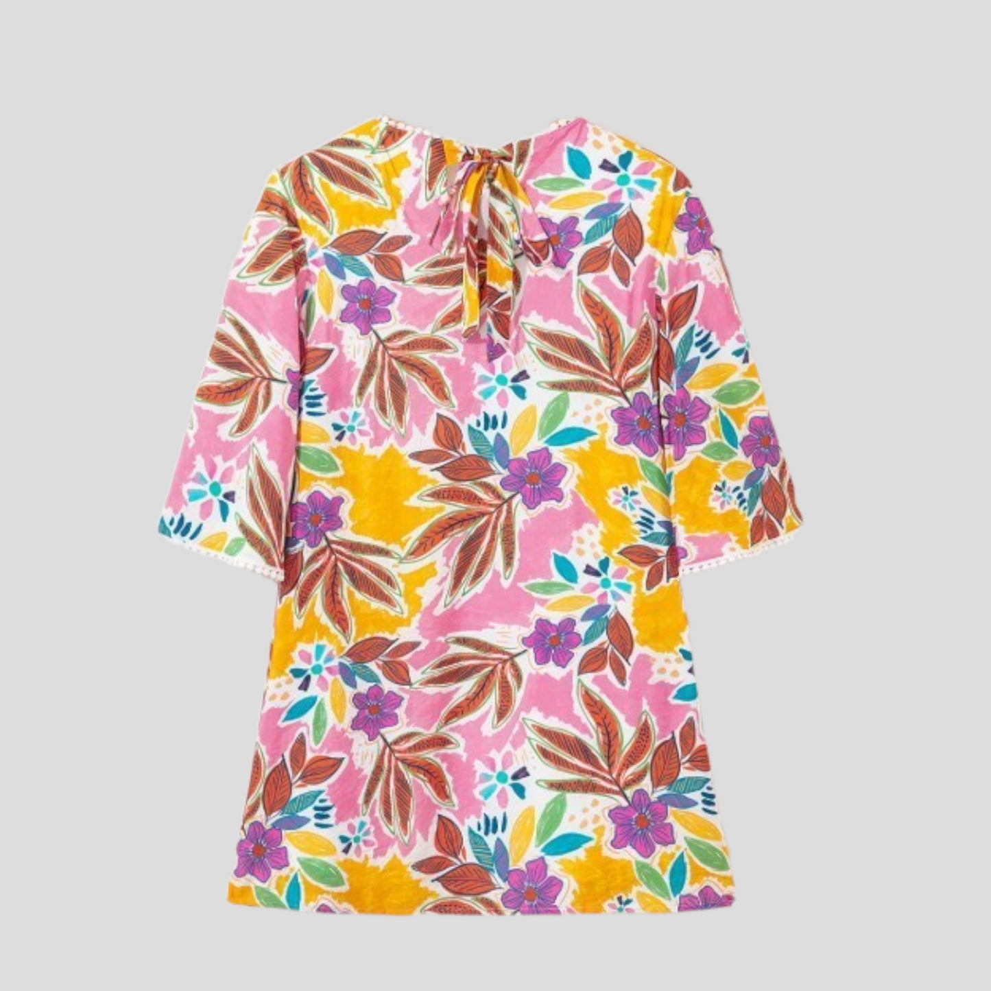Back view flat lay of a colourful tropical floral mini dress featuring a tie-neck closure and pom-pom trim on the sleeves and hem.