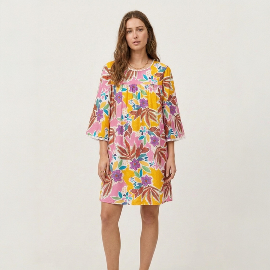Full-length view of a model wearing a tropical floral mini dress with pom-pom trim, styled for a casual summer look.