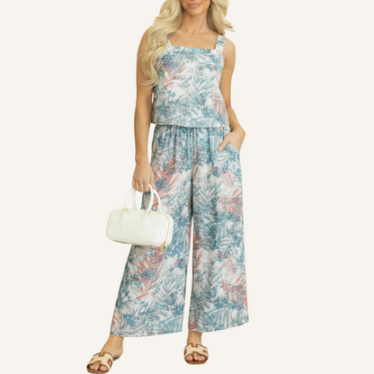 Front view of a woman wearing a two-piece tropical print set featuring a square-neck tank top and matching wide-leg pants with a botanical leaf pattern.