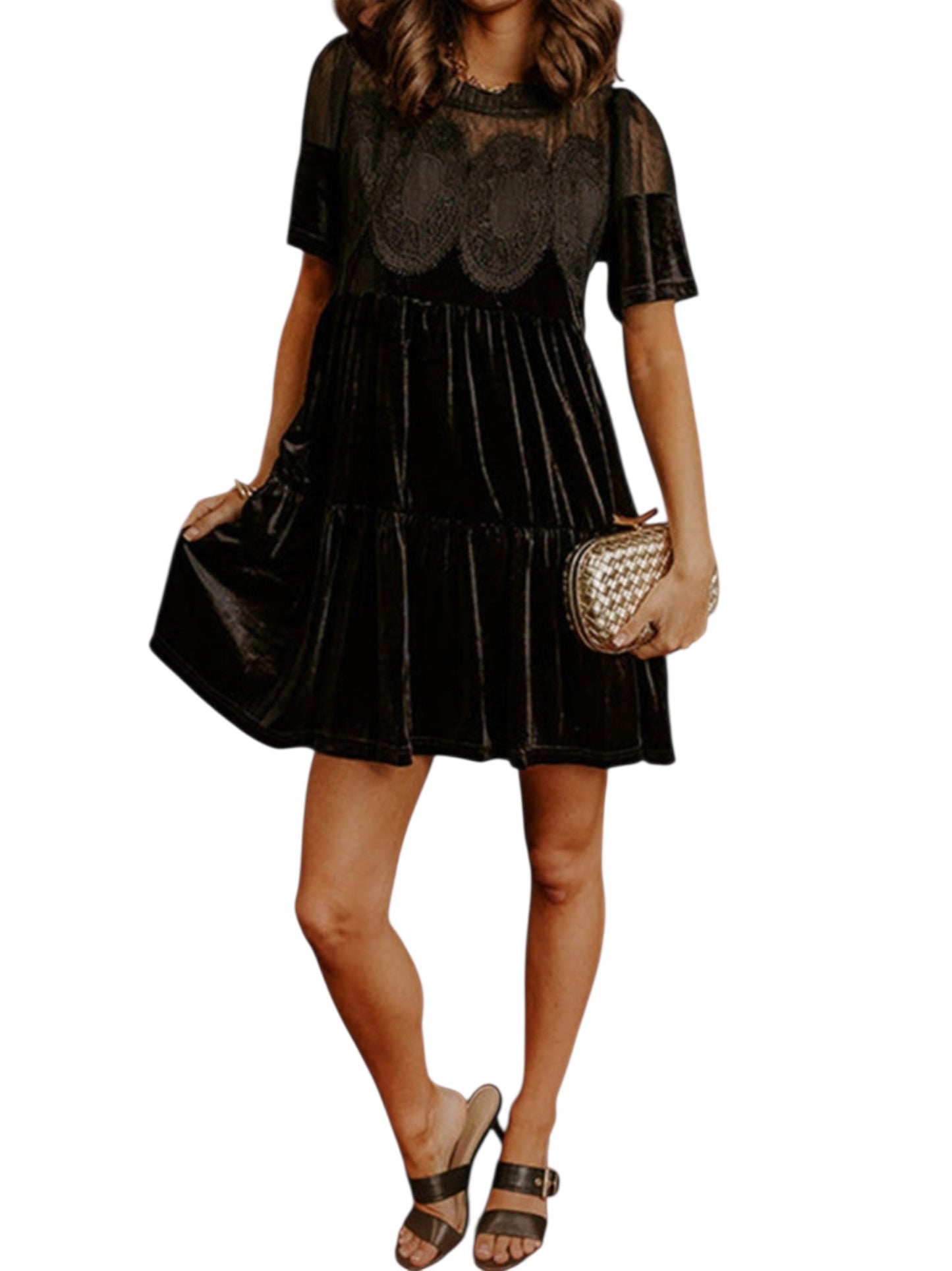 A woman modeling a black velvet tiered mini dress with sheer lace short sleeves and a scalloped lace bodice, holding a small woven clutch against a plain white background.