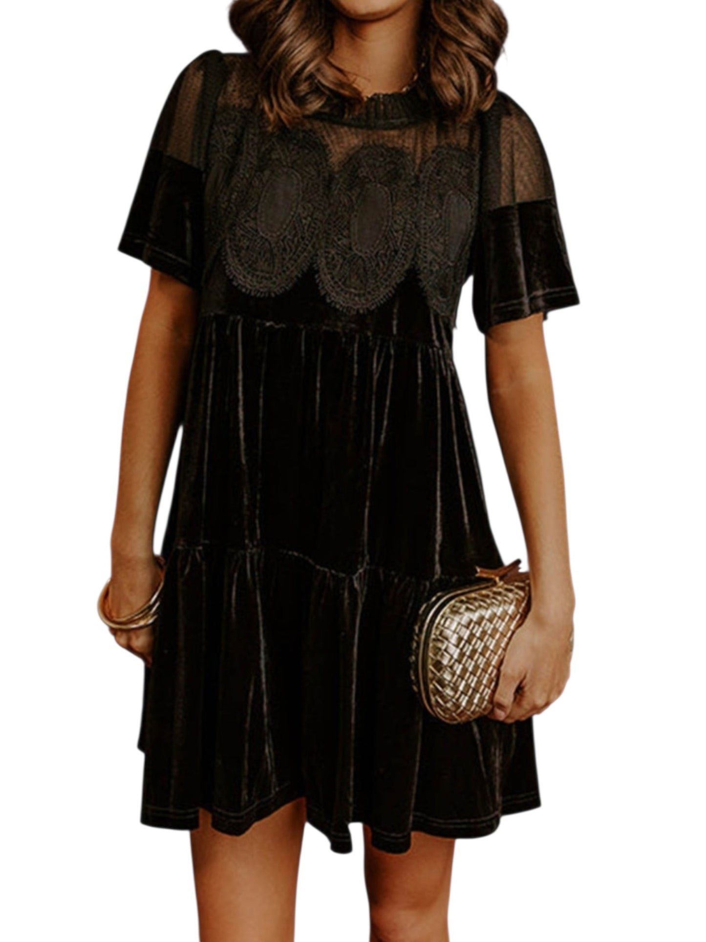 A woman wearing a black short-sleeve velvet dress with sheer mesh sleeves and a scalloped lace yoke, holding a small metallic clutch against a plain white background.