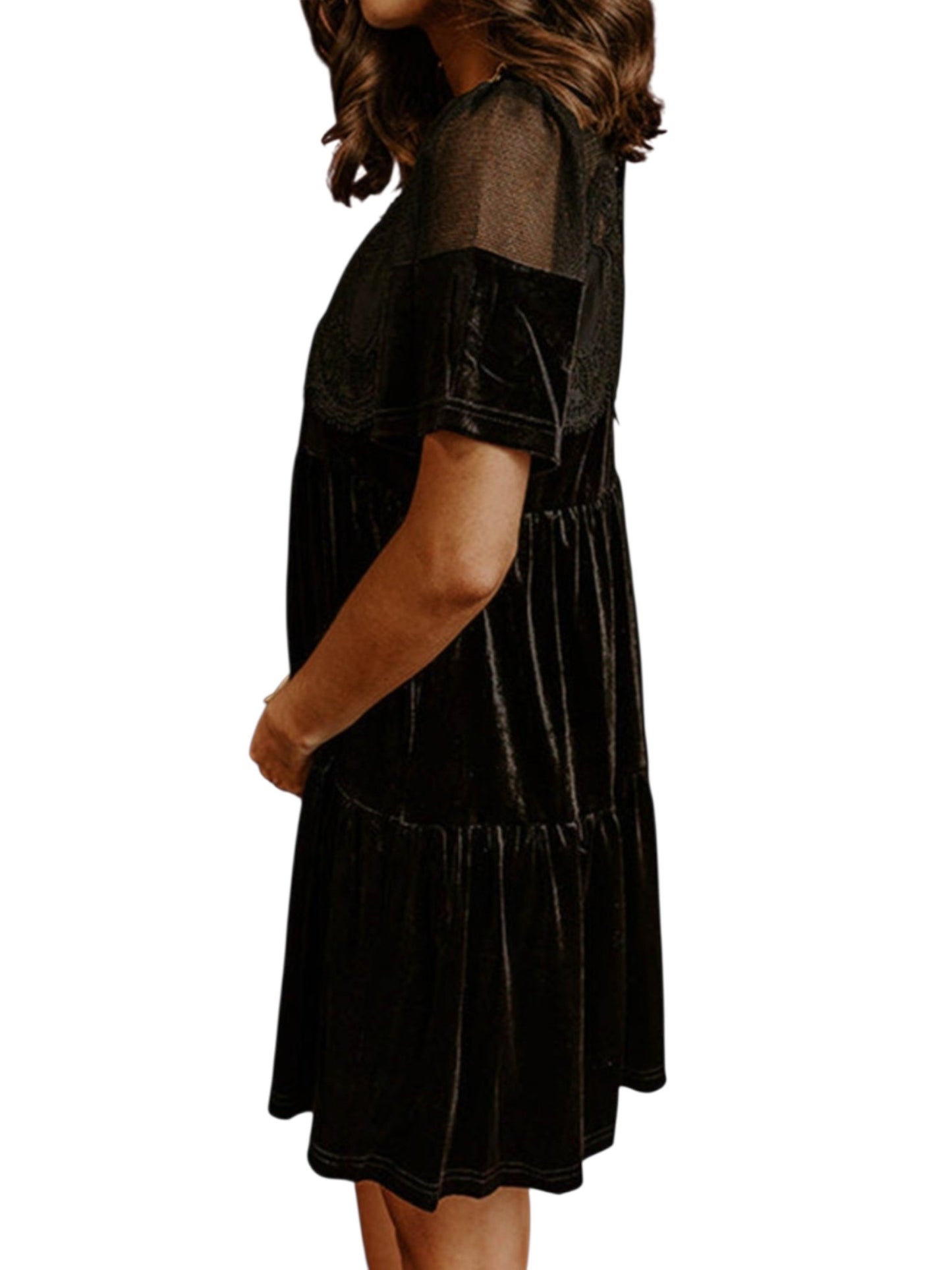 A woman wearing a black tiered velvet dress with sheer short sleeves, shown from a side profile against a plain white background.