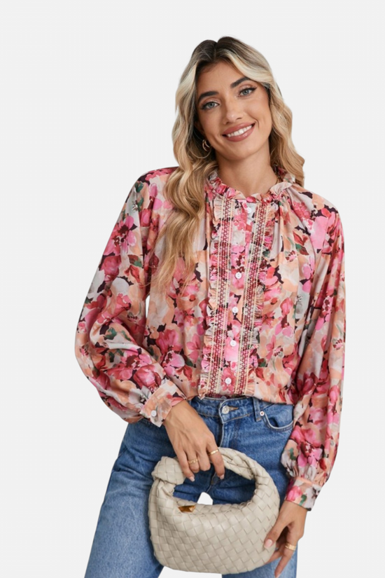 Woman wearing a floral blouse with long sleeves and jeans, holding a beige handbag.