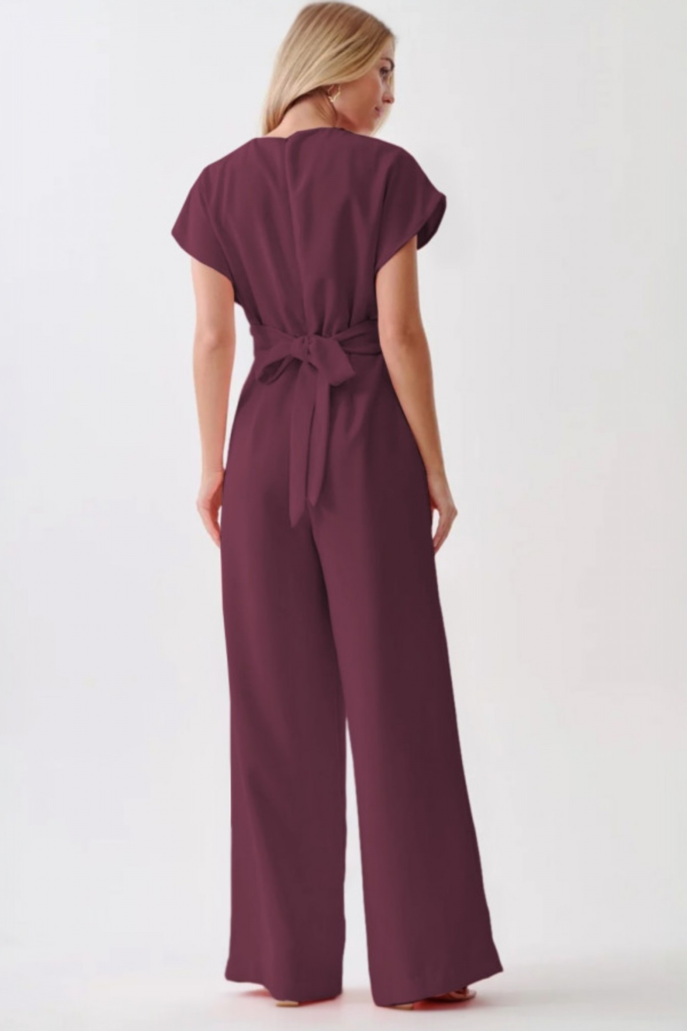 Rear view of a plum wide-leg jumpsuit showing the elegant tie-back knot at the waist and a streamlined, floor-length silhouette.