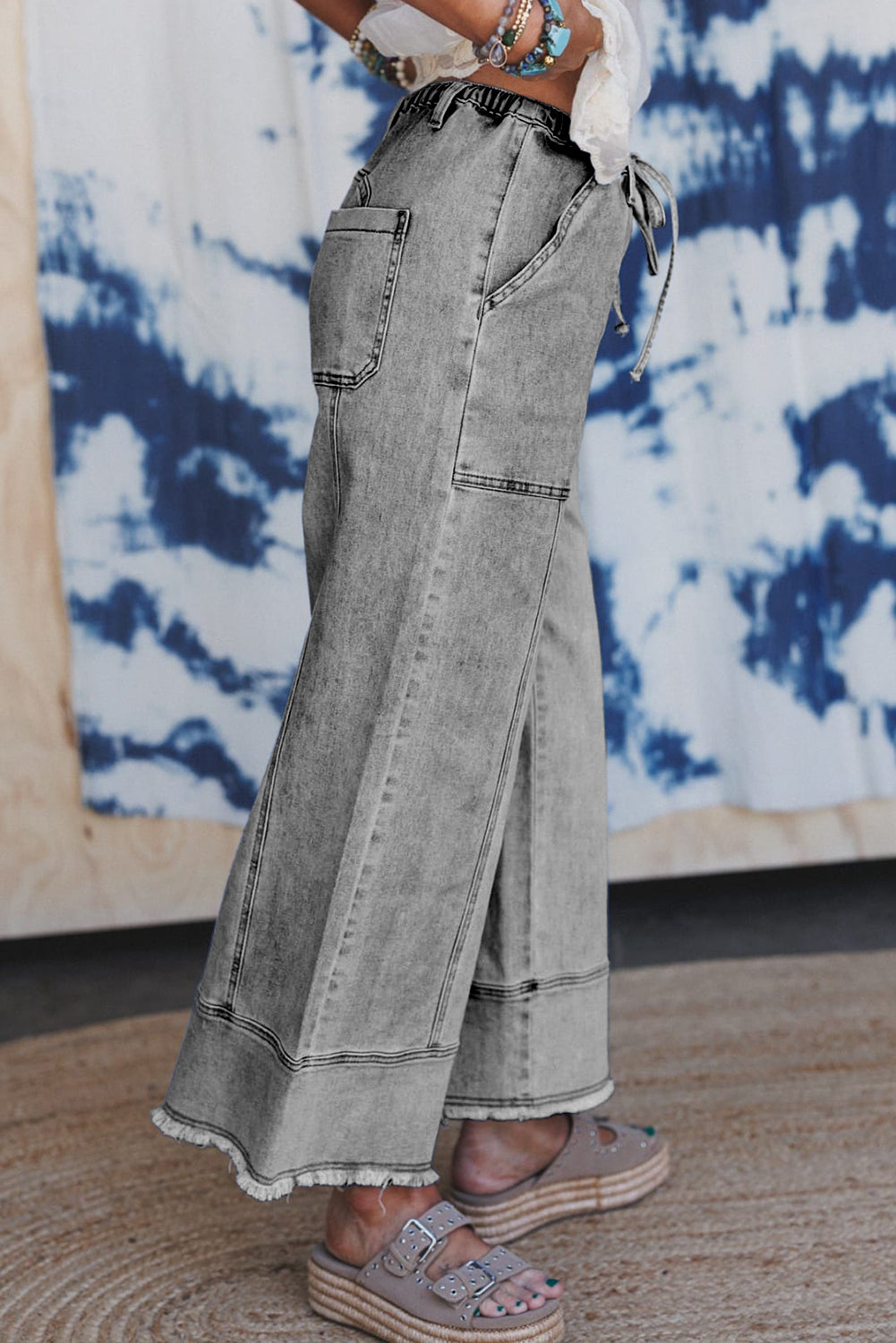 Person wearing wide-leg jeans with a tie-dye wall in the background