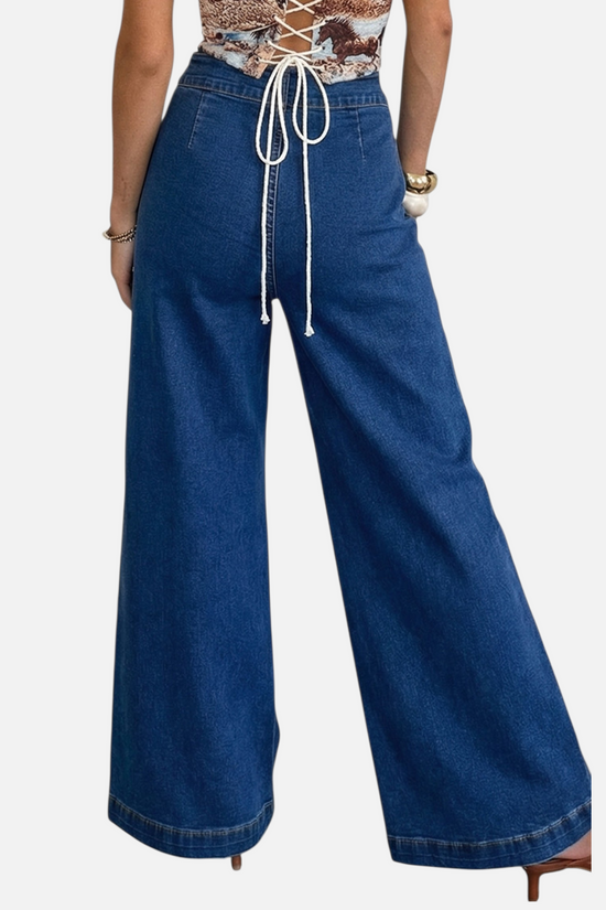 Back view of a  model wearing high-waisted, wide-leg denim trousers featuring metallic hardware accents and functional patch pockets, styled for a modern street-style look.