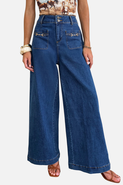A model wearing high-waisted, wide-leg denim trousers featuring metallic hardware accents and functional patch pockets, styled for a modern street-style look.